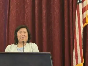 Congresswoman Grace Meng speaking at a podium in front of a red curtain and U.S. flag during the CAPAC reception at NAPABA Lobby Day 2025